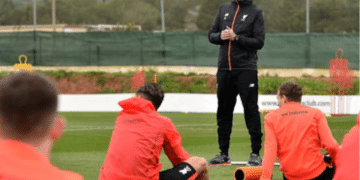 Jürgen Klopp stands to address his football players, who are sat with their backs to camera all wearing the same red jacket, during what he describes as a ‘pre-season training’ camp in La Manga in February 2017