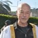 Maher Younis, fomer Palestinian prisoner, has a full grey moustache and bald head. He smiles, the sun shining on him and the white/ gold-trimmed robe over his black shirt