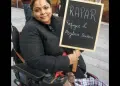 Manjeet Kaur, a human rights campaigner who died, aged 41, in 2020 in Manchester, sought asylum in the UK from Afghanistan in March 2011. In this photo in her wheelchair, she’s smiling holding a chalkboard placard that says 'RAPAR - Refugees and Asylum Seekers'.