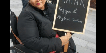 Manjeet Kaur, a human rights campaigner who died, aged 41, in 2020 in Manchester, sought asylum in the UK from Afghanistan in March 2011. In this photo in her wheelchair, she’s smiling holding a chalkboard placard that says 'RAPAR - Refugees and Asylum Seekers'.