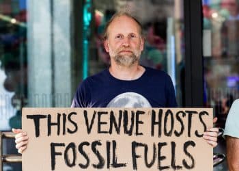 QEII fossil fuel protest Protester holds sign saying This Venue Hosts Fossil Fuels