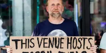 QEII fossil fuel protest Protester holds sign saying This Venue Hosts Fossil Fuels