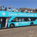 A Reform branded open top double decker bus parked with people on top waving and a woman in the doorway waving too, in 2013