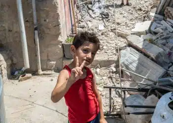 A young boy doing a victory sign in front of rubble in South Lebanon