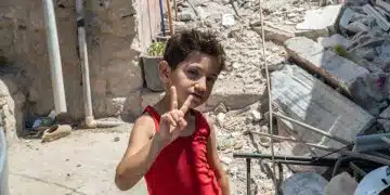 A young boy doing a victory sign in front of rubble in South Lebanon