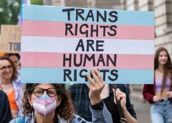 Protester holds a placard in trans pride colours saying Trans Rights Are Human Rights EHRC Code