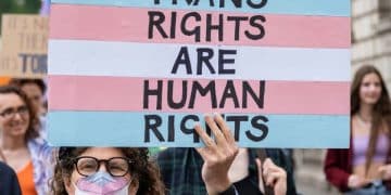 Protester holds a placard in trans pride colours saying Trans Rights Are Human Rights EHRC Code