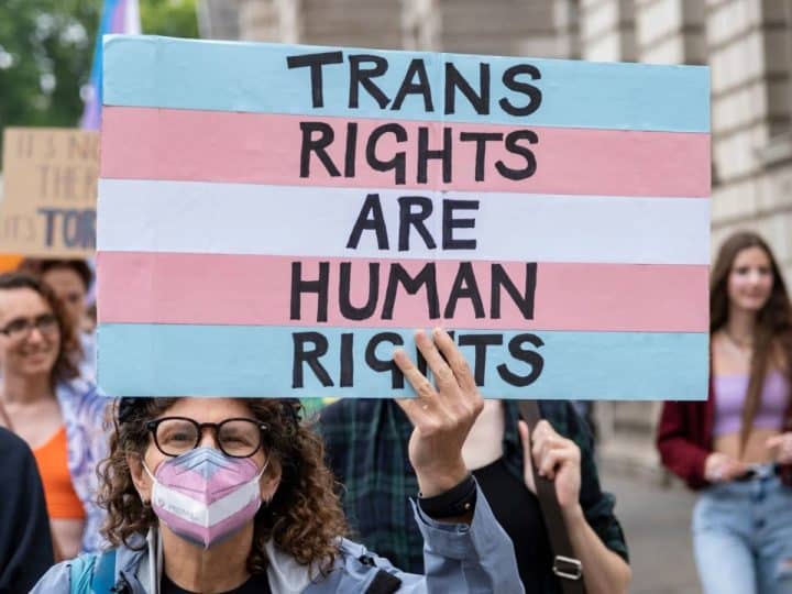 Protester holds a placard in trans pride colours saying Trans Rights Are Human Rights EHRC Code