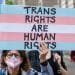 Protester holds a placard in trans pride colours saying Trans Rights Are Human Rights EHRC Code