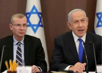Yariv Levin (left) and Benjamin Netanyahu sat next to one another with mics infront of them and there is the star of Israel on decorations behind them