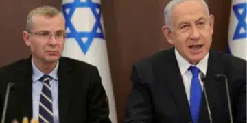 Yariv Levin (left) and Benjamin Netanyahu sat next to one another with mics infront of them and there is the star of Israel on decorations behind them