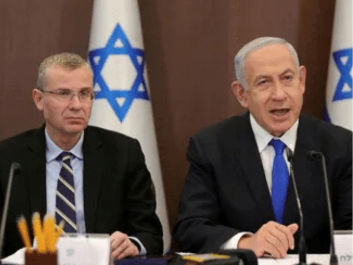 Yariv Levin (left) and Benjamin Netanyahu sat next to one another with mics infront of them and there is the star of Israel on decorations behind them