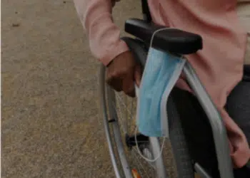 Close-up of the hand of a black woman pushing her wheelchair, she put her surgical face mask on the armrest. Police have warned unwell campaigners their health is not an automatic pass for wearing a face mask.