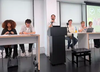 Young Greens party conference. Each candidate is sat at the front of a classroom on two desks with a podium and mic in the middle, where one candidate is speaking